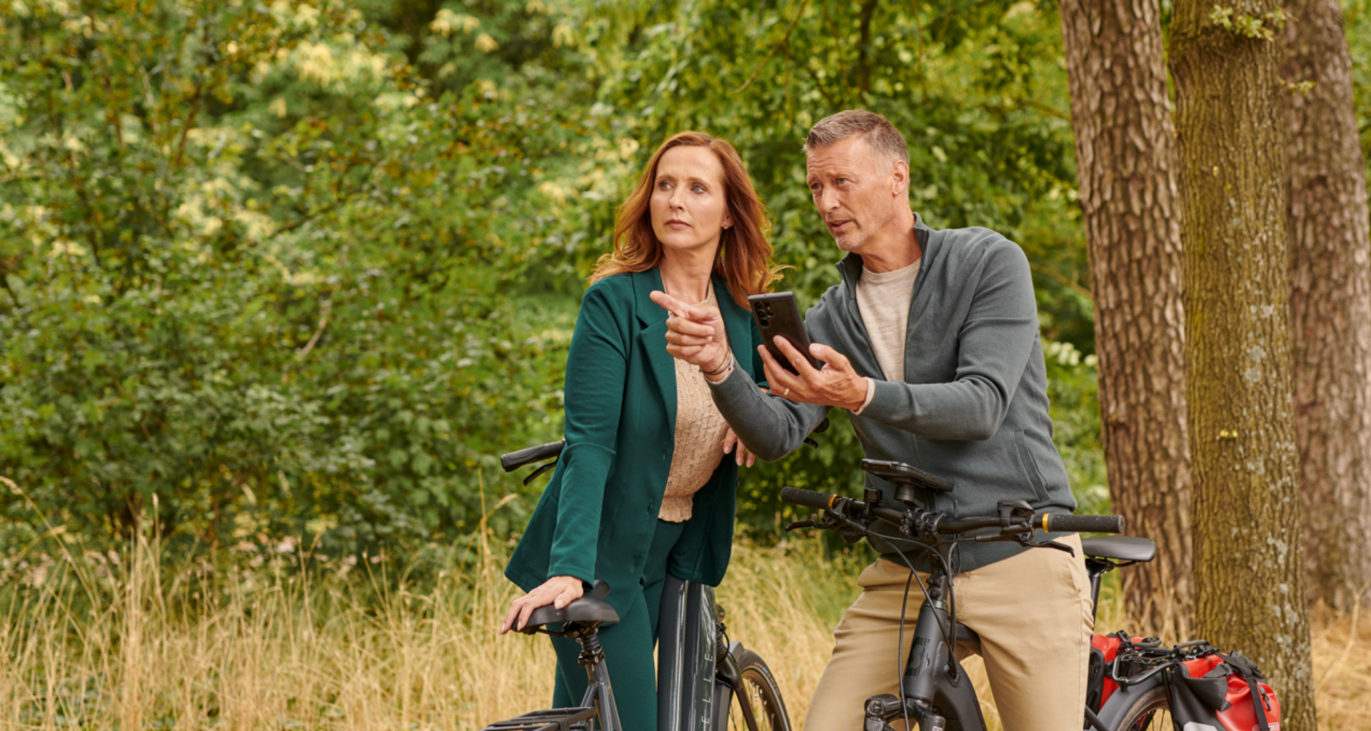 Man en vrouw van middelbare leeftijd staan stil met de e-bike en kijken op hun mobiel om te zien of ze nog op de juiste weg zijn.