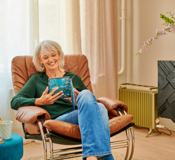 Een vrouw zit in een comfortabele stoel en leest een boek op een e-reader.